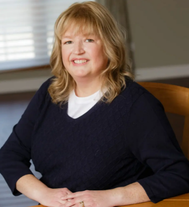 Althea Olson in a dark sweater and white shirt, sitting with clasped hands